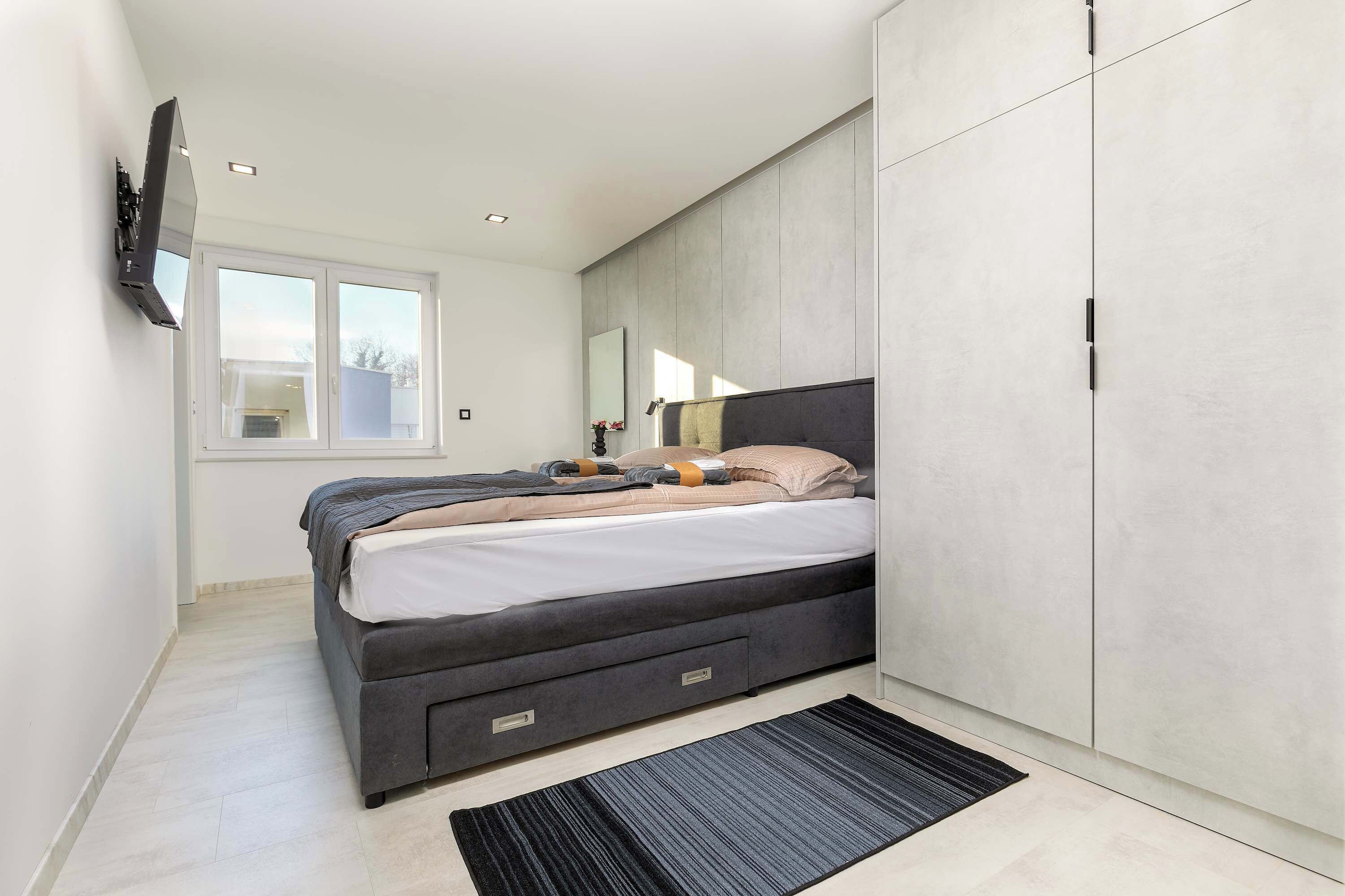 A modern bedroom with a bed, wardrobe, and a flat-screen TV mounted on the wall.