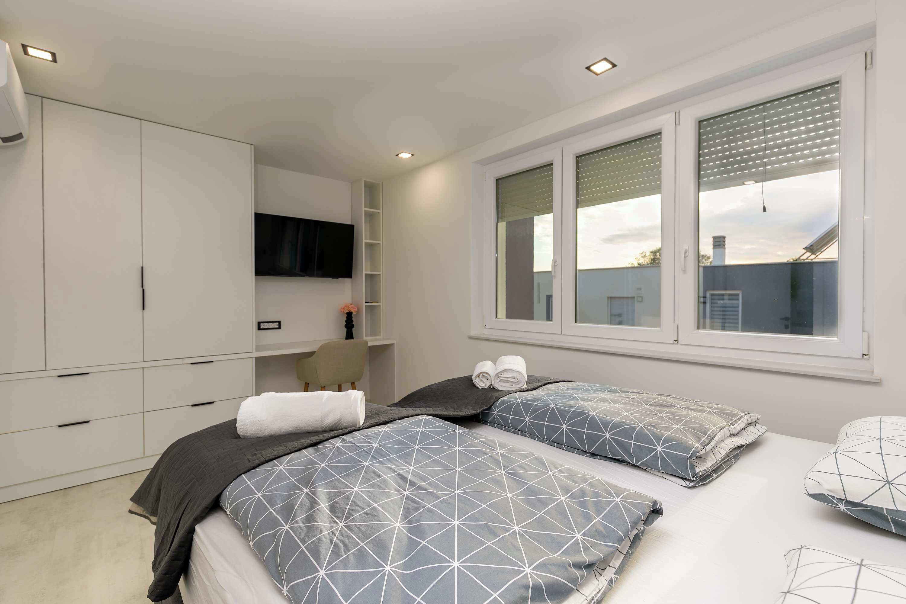 Um quarto com cama, televisão, guarda-roupa e janela.