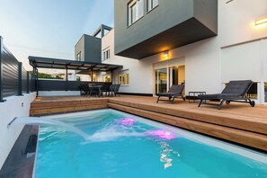 A modern outdoor pool area with a wooden deck, lounge chairs, and a covered seating area. - Villa Franka with pool near Medulin (Ližnjan)