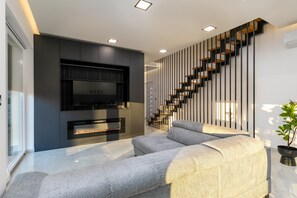A modern living room with a fireplace, a grey sofa, a staircase with black railings, and a potted plant. - Villa Franka with pool near Medulin (Ližnjan)