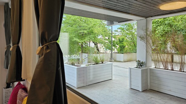 Una habitación moderna con ventanas amplias, techo de madera y vistas a un jardín con macetas.