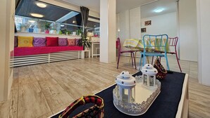 Una sala moderna con piso de madera, un sofá rojo con cojines estampados, una mesa de comedor con sillas coloridas y faroles decorativos.