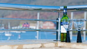 A bottle of Firestone Vineyards Merlot wine and two wine glasses on a railing with a view of a harbor and hills in the background. - Quay Lodge (Dartmouth)