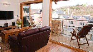 A modern living room with a large window, a flat-screen TV, a leather sofa, and a wooden coffee table. - Quay Lodge (Dartmouth)