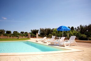 Une piscine avec des chaises longues blanches et un parasol bleu.
