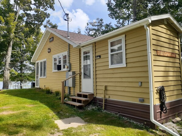 A single-story mobile home with a brown roof and beige siding, featuring a front porch and a small deck. - Cozy 1 Bdrm cabin/sleeps 4. Fireplace/Lakefront/Kayaks and pedal boat included (Remus)