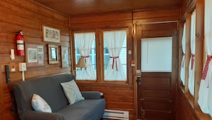 Een knus cabin interieur met houten details, een grijze bank met kussens, een brandblusser en een deur met gordijnen.