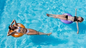 Dos personas flotando en una piscina azul cristalina con anillos inflables.