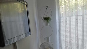Et værelse med et fjernsyn ophængt på væggen, et skrivebord med en bærbar computer, en ventilator og en lille plante på en piedestal.