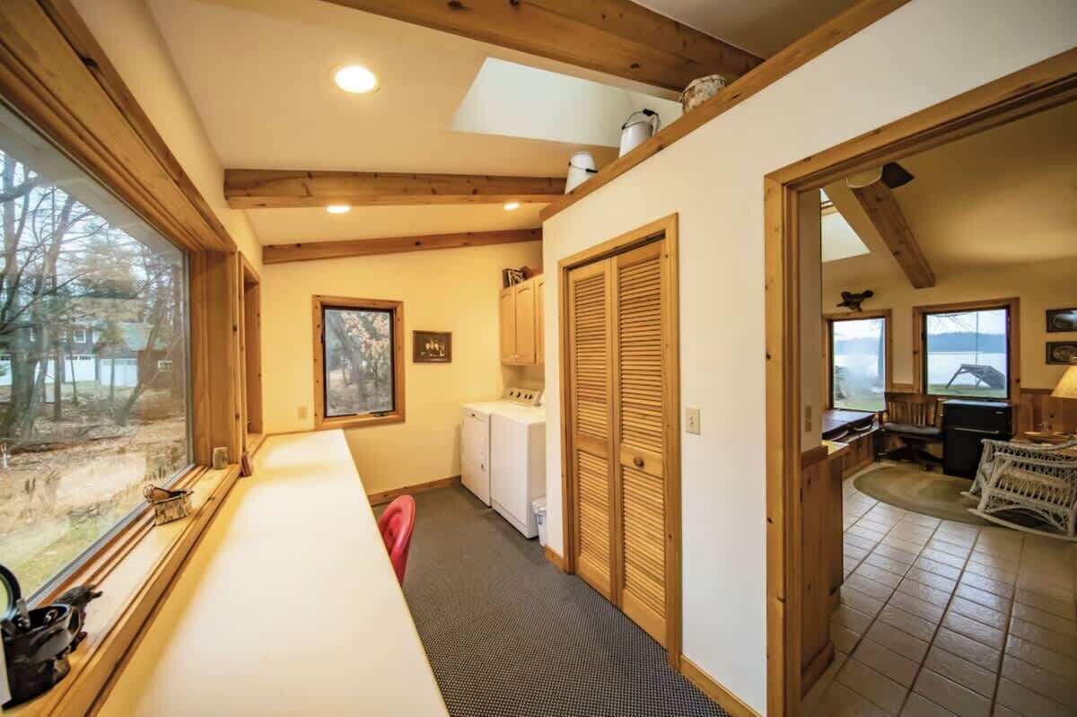 Een kleine kamer met een groot raam, een wasmachine en een houten deur.