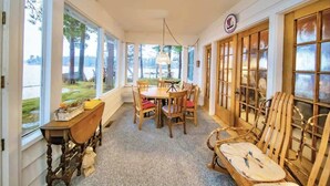 A room with a wooden table and chairs, large windows, and a view of the outdoors. - Pines of Three Lakes (Eagle River)
