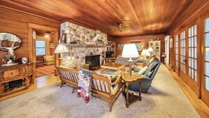 A cozy living room with a stone fireplace, wooden furniture, and large windows. - Pines of Three Lakes (Eagle River)