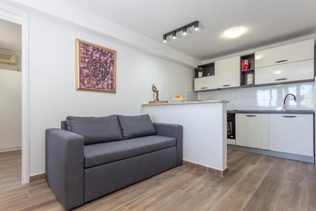 Una cocina moderna con armarios blancos, un sofá gris y un cuadro abstracto enmarcado en la pared.