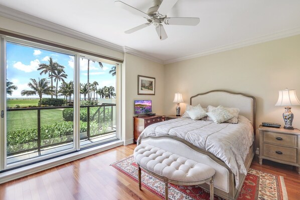 A bedroom with a large sliding glass door leading to a balcony, a bed with a headboard, two bedside tables with lamps, and a television.