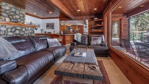 A cozy living room with a leather sofa, a coffee table, and a view of the outdoors through large windows.