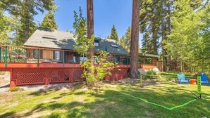 A cabin with a deck, surrounded by trees and a grassy yard.