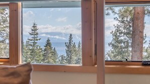 A room with a large window, wooden beams, and a view of trees and mountains.