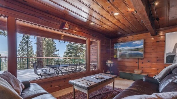 A wooden interior with a leather sofa, a coffee table, and a view of the outdoors.