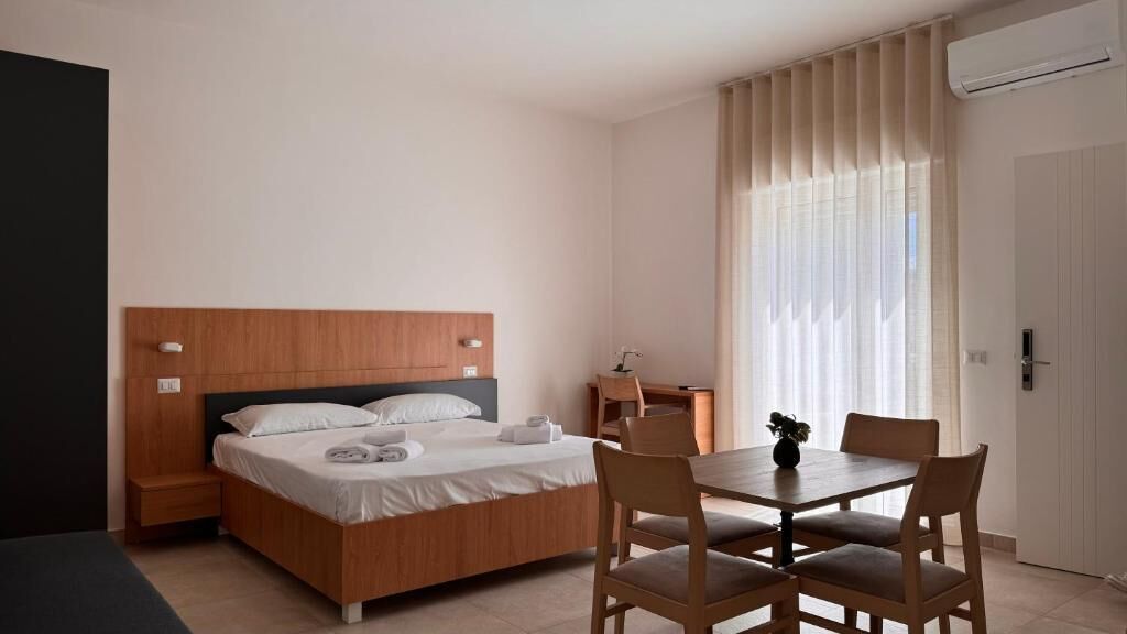 A hotel room with a wooden bed, a small desk, a chair, and a dining table.