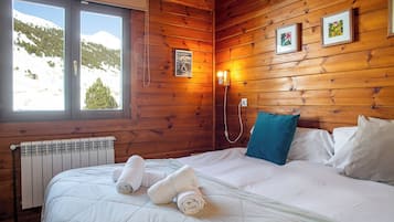 A wooden cabin room with a bed, two pillows, a radiator, and framed pictures on the wall.