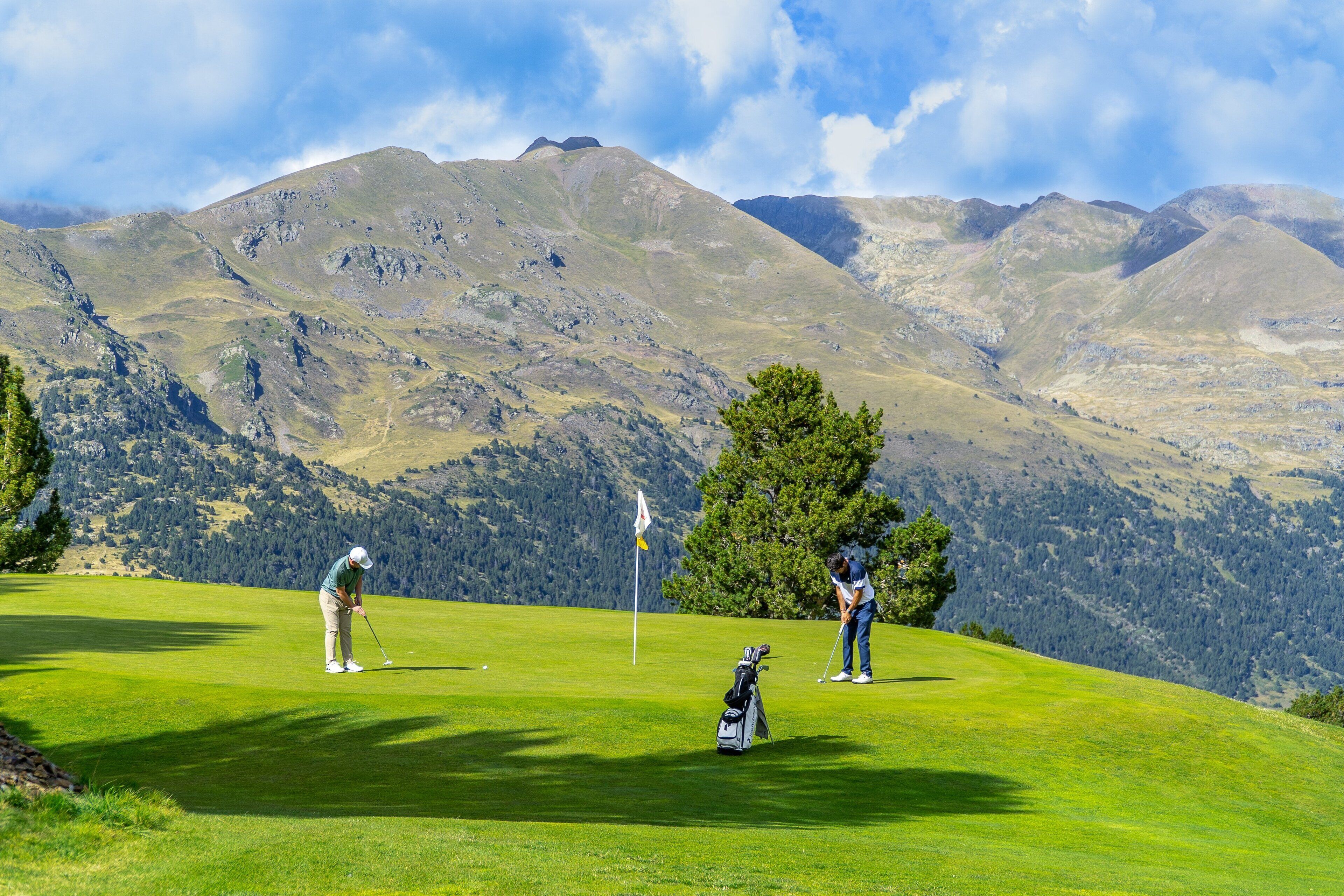 A golf course with two players, a flagstick, and a bag of golf clubs.