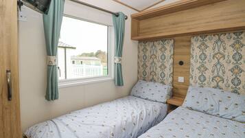 Een compacte slaapkamer met twee eenpersoonsbedden, een aan de muur bevestigde televisie en een raam met gordijnen.