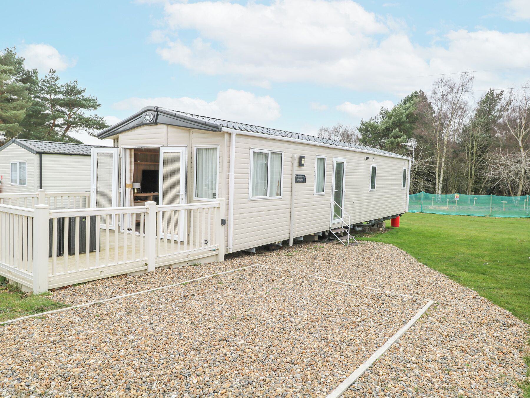 A mobile home with a deck, a small porch, and a gravel driveway.