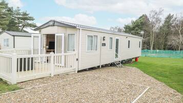 A mobile home with a deck, a small porch, and a gravel driveway.