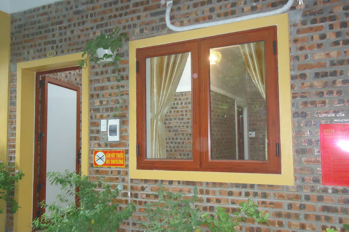 Un bâtiment en briques avec deux fenêtres à cadre en bois, une porte et un panneau indiquant qu’il est interdit de fumer.