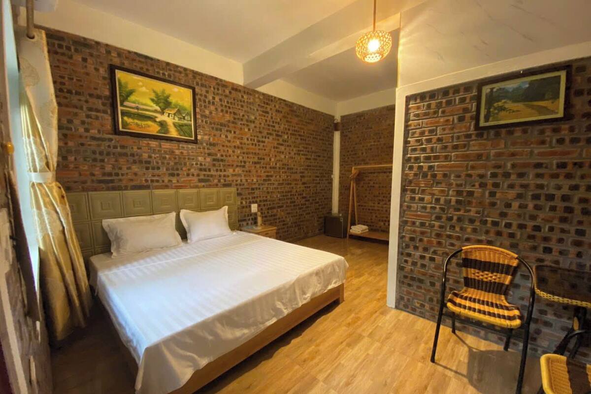 Une chambre avec un grand lit, un plancher en bois, un mur en briques et un luminaire suspendu.