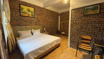 A bedroom with a large bed, a wooden floor, a brick wall, and a hanging light fixture.