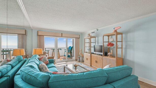 A modern living room with teal sofas, a glass coffee table, and a TV on a wooden cabinet.