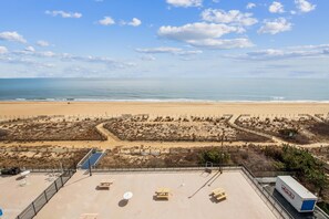 A beach view with a clear sky, sandy beach, and a parking area with picnic tables and a solar panel.