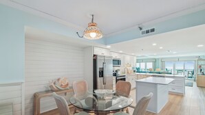 A modern kitchen with white cabinetry, a central island, and a dining area with wicker chairs.
