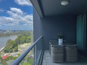 A balcony with wicker furniture, a potted plant, and a view of a river and cityscape.