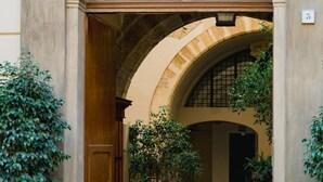 Une entrée en arc surmontée d’une porte en bois, agrémentée de plantes en pot et d’un chemin de pierre menant à une cour intérieure.