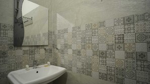 Ein Badezimmer mit weißem Waschbecken, einem Spiegel und Wandfliesen mit Muster.