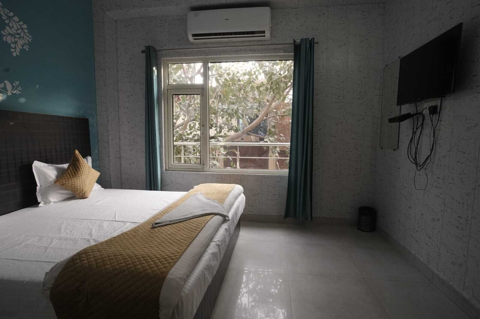 Une chambre à coucher avec un lit, une fenêtre avec des rideaux, un appareil de climatisation et un téléviseur fixé au mur.