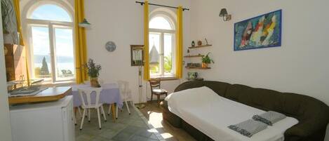 Una habitación acogedora con una cama, un escritorio y una silla. Hay ventanas con cortinas, un reloj y un cuadro en la pared.