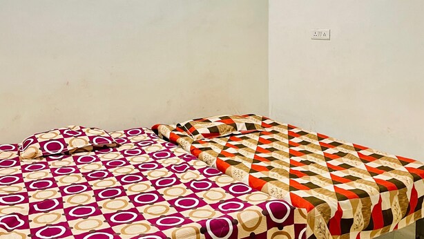 Two beds with patterned bedding in a room with a plain wall and a visible electrical outlet. - Om Sai guest house (Varanasi)