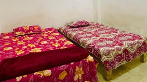 Two single beds with floral-patterned bedding in a room with plain walls and a tiled floor. - Om Sai guest house (Varanasi)