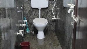 A small, narrow bathroom with a toilet, a sink, and a shower area. - Om Sai guest house (Varanasi)