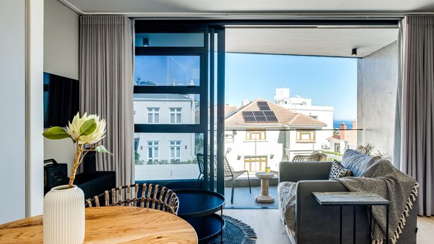 A modern living room with a large window, a dining table, and a sofa. - Central Secure Modern Studio w Views Bantry Pad (Cape Town)
