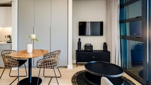 A modern living room with a round wooden table, wicker chairs, a black sofa, a black console table with a TV, and a large window with curtains. - Central Secure Modern Studio w Views Bantry Pad (Cape Town)