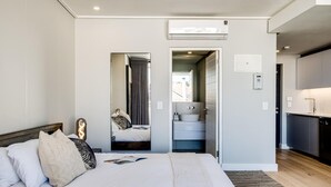 A modern hotel room with a large bed, a bedside table, a mirror, a bathroom with a sink and toilet, and a kitchen area. - Central Secure Modern Studio w Views Bantry Pad (Cape Town)