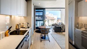 A modern kitchen with white cabinets, a black countertop, and a dining area with a round table and chairs. - Central Secure Modern Studio w Views Bantry Pad (Cape Town)