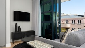 A modern living room with a grey sofa, a black TV on the wall, a black console table with decorative items, and a view of buildings through large windows. - Central Secure Modern Studio w Views Bantry Pad (Cape Town)