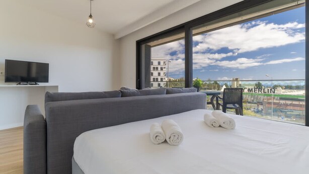 Una habitación de hotel moderna con una cama grande, un televisor de pantalla plana y un balcón con vistas a la ciudad.