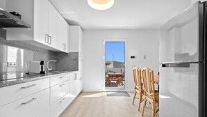 Une cuisine moderne avec des meubles blancs, un four encastré et un coin repas comprenant une table et des chaises.