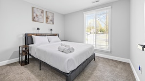 A bedroom with a bed, two bedside tables, a window with blinds, and two wall-mounted lamps. - Quail Ridge 3BR House (Charlotte)